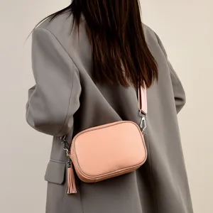 Detail view of a stylish pink leather camera crossbody bag with wide strap and tassel.