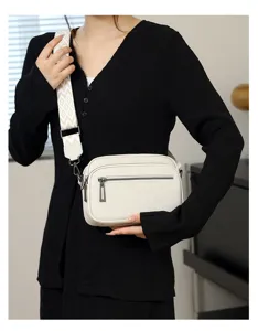 Élégant sac bandoulière en cuir blanc avec large sangle à motifs et double fermeture éclair.