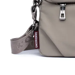 Detail view of the lightweight nylon shoulder bag strap, hardware, and branded tag.