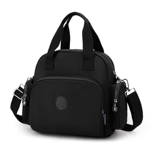 Black nylon shoulder bag detail showing sturdy top handles, durable fabric and zipper pocket.