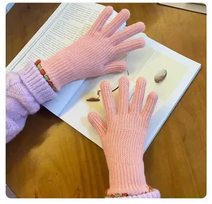 Detail shot of cozy pink knit five-finger gloves with cute colorful cuff trim on book background.