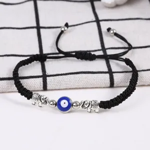 Gros plan sur les perles mauvais œil bleu et éléphants argentés du bracelet tressé noir.