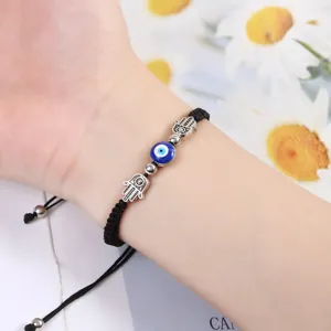 Gros plan détaillé d'un bracelet en cordon noir tressé avec des amulettes de main de Fatima et œil.