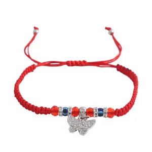Détail de bracelet en corde rouge tressée, avec charm papillon en cristal et perles mauvais œil.