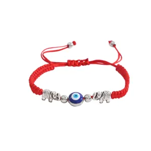 Gros plan détail du bracelet cordon tressé rouge avec perle mauvais œil et breloques éléphant.