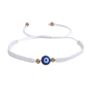 Gros plan sur le bracelet tressé blanc avec un œil turc porte-bonheur et perles dorées.