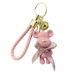 Détail du porte-clés ours en peluche rose avec lanière tressée et accessoires.