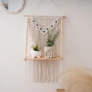 Handmade macrame wall hanging shelf with wooden beads and evil eye decor for home.
