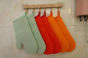 Silicone oven mitts detail showing heat-resistant textured design hanging on wall hook.
