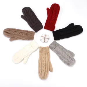 Detailed view of thick cable knit mittens in multiple colors arranged nicely with cotton.