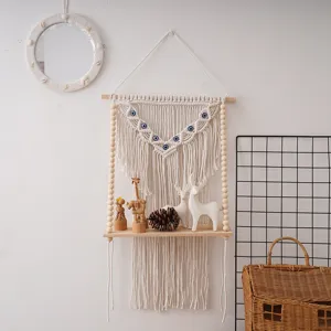 Handmade macrame wall hanging shelf with wooden beads and evil eye design for room decor.