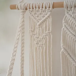 Close-up of handmade woven macrame wall hanging with intricate knotting details on wooden rod.