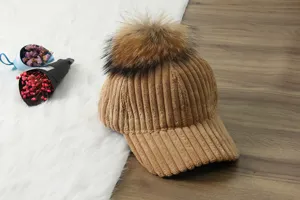 Corduroy baseball cap detail view featuring a large fluffy pom-pom and ribbed brim texture.