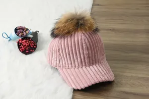Pink corduroy baseball cap with a large fluffy pom-pom detail for cozy autumn and winter.
