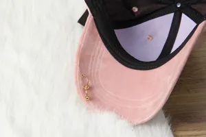 Close-up detail of pink corduroy baseball hat featuring stylish metal piercing rings on brim.