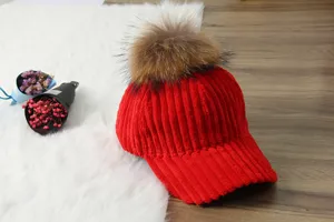 Red corduroy baseball cap detail view showing the soft fabric texture and fluffy fur pom pom.