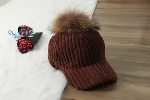 Detailed view of the brown corduroy baseball cap featuring a fluffy fur pom pom on top.