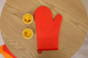 Silicone oven mitt detail shot, heat resistant baking glove with textured grip, red.