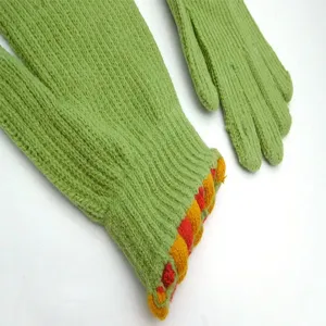 Close-up detail of winter green knitted gloves with colorful pom-pom cuffs, warm fabric.