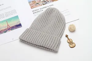Detail view of a cozy light grey knitted winter beanie hat in a stylish flat lay setup.