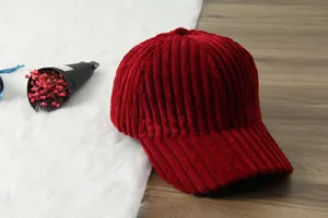 Red corduroy baseball cap detail view, soft fabric texture and curved brim close-up.