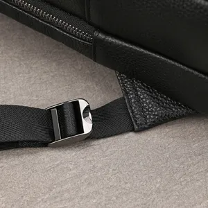 Close-up detail of black genuine leather backpack showing fine texture, zipper and metal buckle.