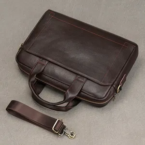 Dettaglio della borsa da lavoro in pelle marrone, borsa per laptop resistente e manici robusti.