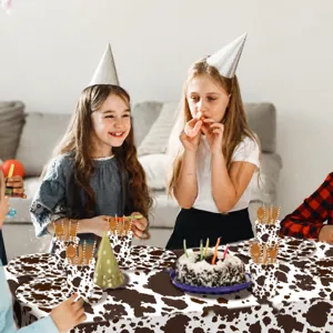 Cow print birthday party tablecloth and disposable tableware set for kids farm theme celebration.