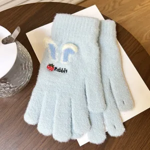 Gros plan détaillé de gants en tricot bleu clair avec oreilles de lapin et broderie.