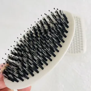 Oval men's beard brush detail showing mixed bristles and white handle for daily hair styling.