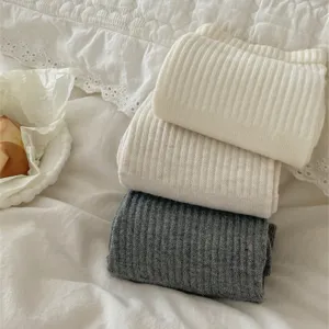 Close-up detail of cozy knit wool over-the-knee leg warmers, soft texture on white bedding setup.