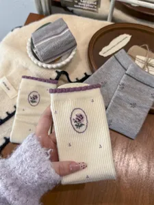 Detail van gezellige gebreide sokken met delicate vintage blozenborduurwerk en geribbelde boorden.
