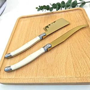 Detalle del juego de cuchillos para mantequilla dorados con mango blanco elegante.