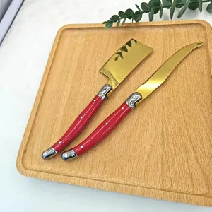 Cuchillo de queso dorado y espatula de mantequilla con mango rojo, vista detallada.