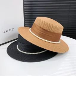 Detail view of elegant women's flat top straw hat with pearl decor and ribbon for summer beach.