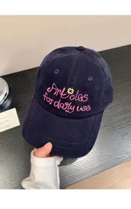 Closeup of dark blue baseball cap featuring pink embroidered letters and cute flower detail.
