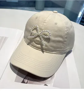 Close-up detail of the elegant beige baseball cap featuring a delicate pearl bow design.