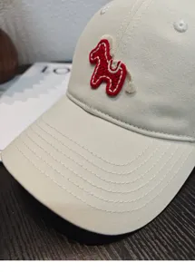 Primo piano di berretto da baseball beige con grazioso motivo di cavallo ricamato rosso.
