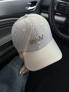 Close-up detail of stylish striped baseball cap with cute Shhh embroidery and curved brim.