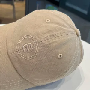 Nahaufnahme einer beige Baumwoll-Baseballkappe mit gesticktem m-Logo, strukturierter Stoff.