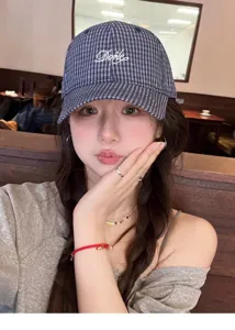 Close-up detail shot of a stylish plaid baseball cap worn by a model in a cozy cafe setting.