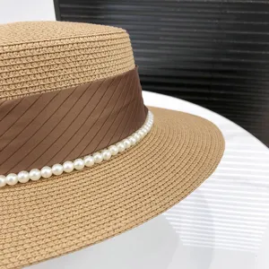Women's flat top straw hat with brown ribbon and pearl decoration for summer sun protection.