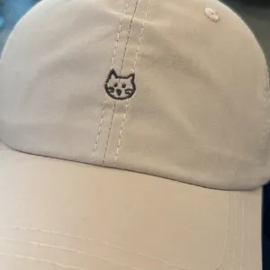 Closeup of beige baseball cap featuring cute cat face embroidery detail, minimalist style.