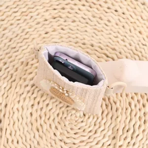 Gros plan du mini sac bandoulière en paille tissée pour téléphone avec joli décor floral et cordon.
