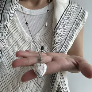 Detailed view of long titanium steel sweater chain with hammered heart pendant and bead accents.