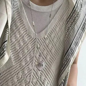 Detail shot of a long stainless steel sweater chain featuring a hammered heart pendant and white bead accents.