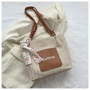 Detail shot of woven straw tote bag with brown PU pocket and braided shoulder strap.