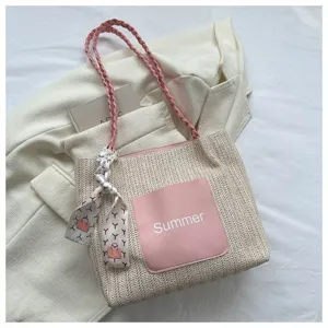 Stylish woven straw tote bag for women featuring pink braided handles and front pocket detail.
