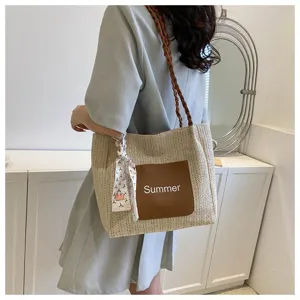 Close-up of stylish straw woven shoulder tote bag with brown front pocket and scarf detail.
