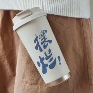 Detailed shot of portable stainless steel insulated coffee cup with strap and slogan.